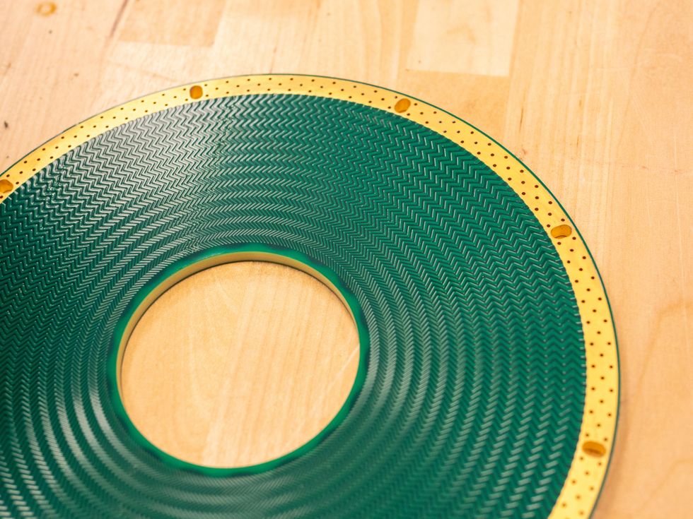A photo of a printed circuit board stator, a thin green disc with a hole in the middle.