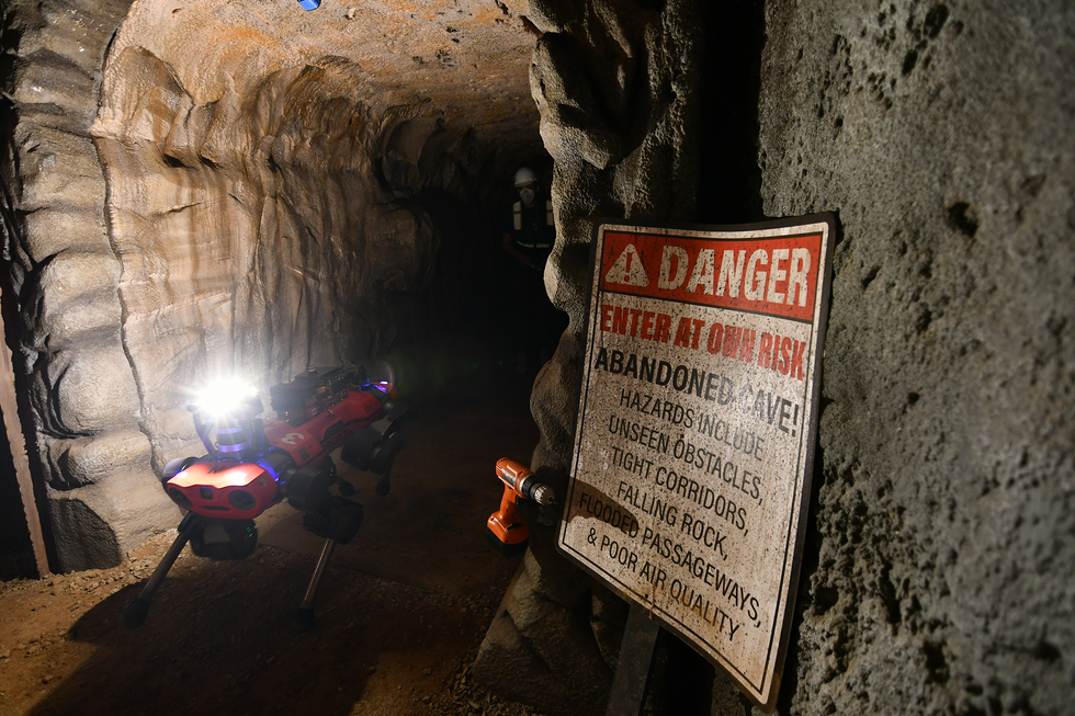 A photo of a quadruped moving through a cavern next to a sign that says u201cDANGER, Enter at your own risk.u201d