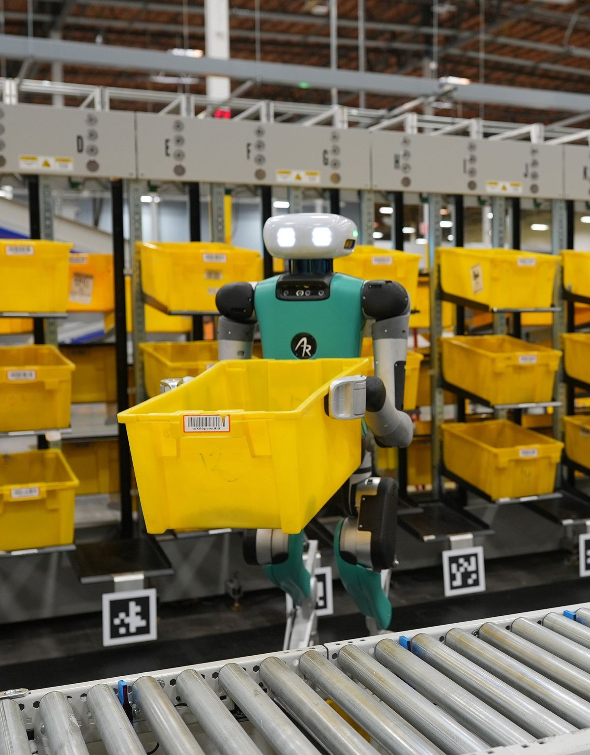 A photo of a robot holding a container in front of rows of containers.