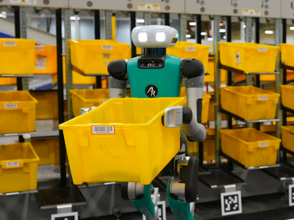 A photo of a robot holding a container in front of rows of containers.