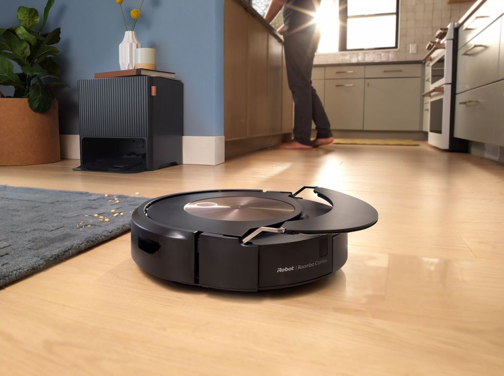 A photo of a Roomba vacuuming robot on a living room floor as it lifts up its mopping pad before driving onto carpet.