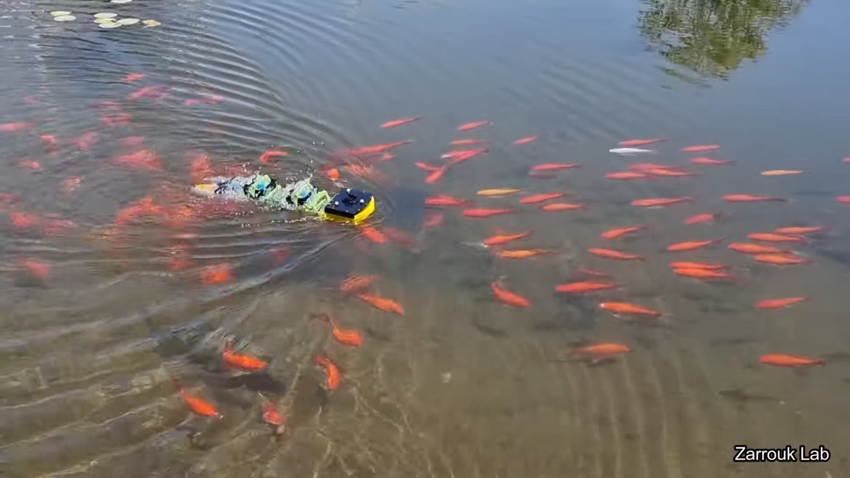 A photo of a small yellow robot swimming in a fish pond, surrounded by goldfish