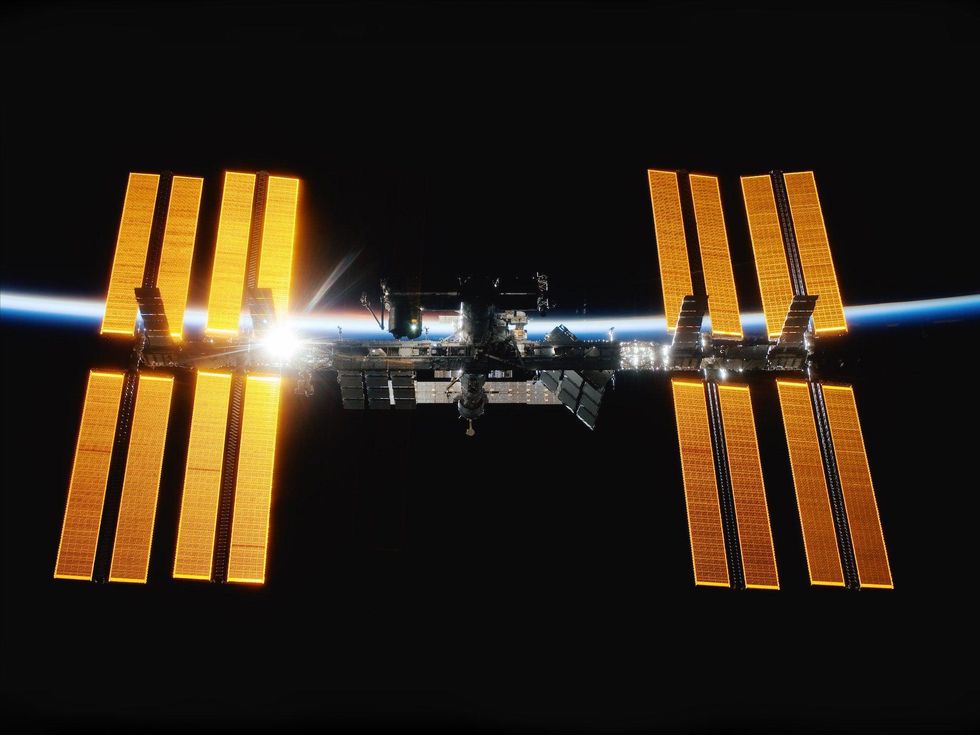 A photo of the ISS, as a sunrise shines through one of the 16 solar panel housings flanking the space station's central modules.
