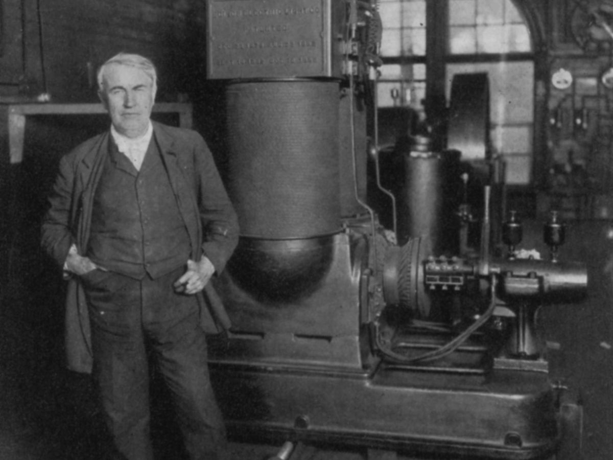 A photo of Thomas Alva Edison standing in front of a dynamo.  