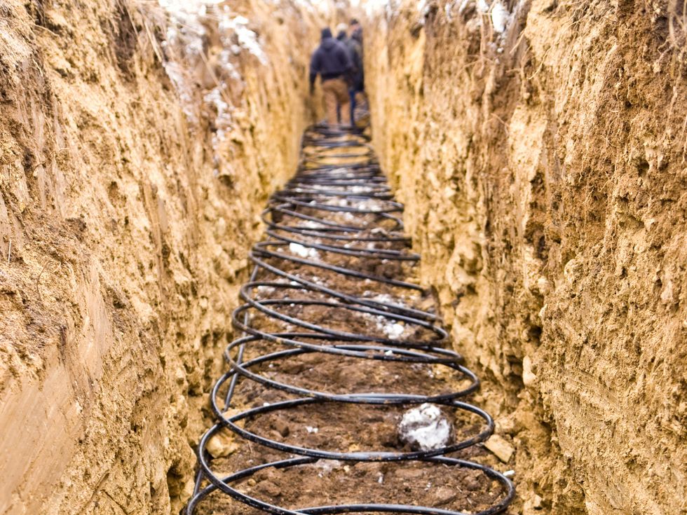 A photo of three men in a trench at the bottom of which is coiled black tubing.