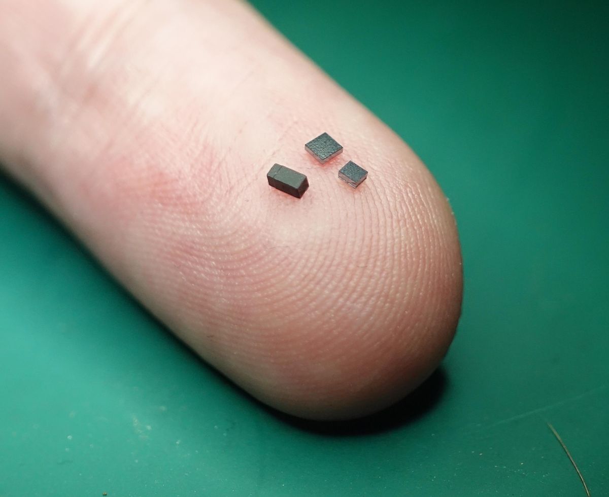 A photo of three tiny black electronic components on a fingertip