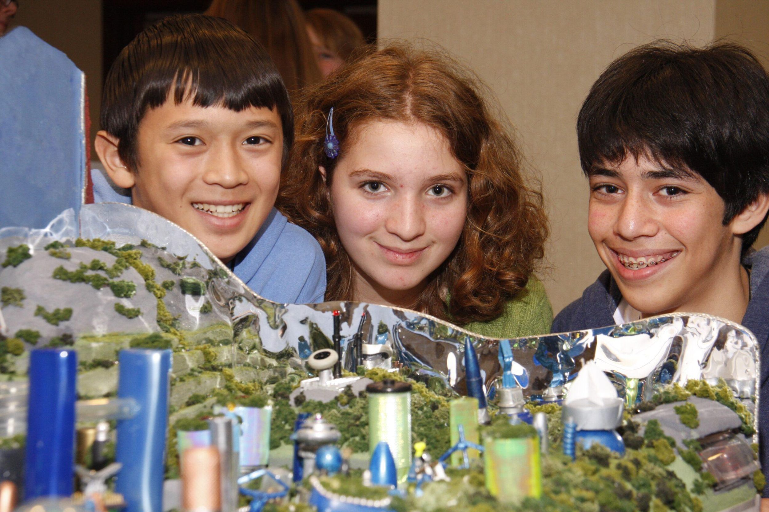 A photo of two boys and a girl with a display in front of them.  
