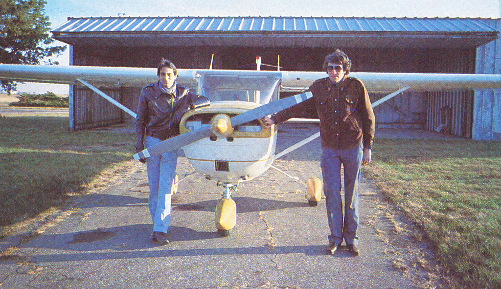 A photo of two men standing next to a prop plane.