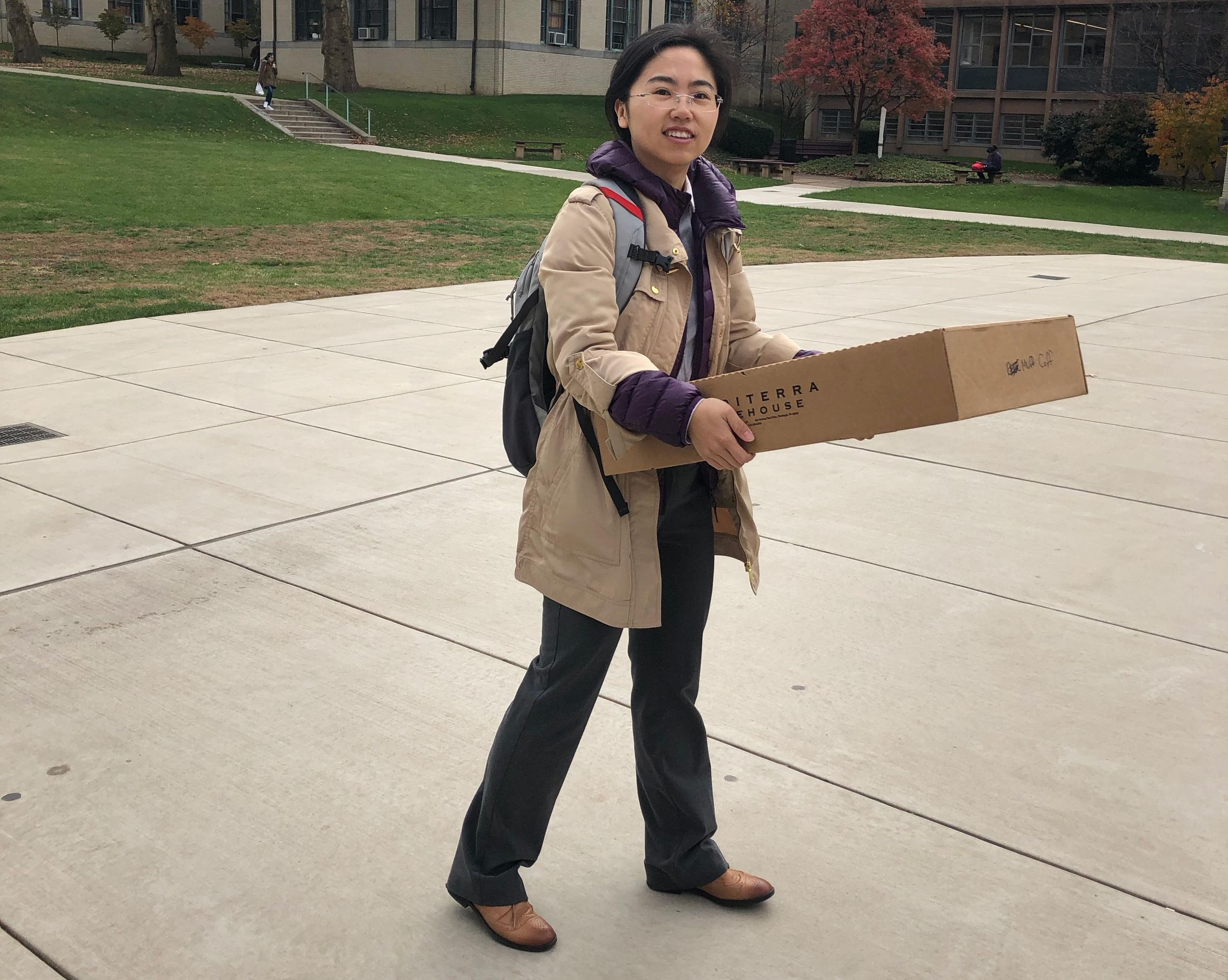 A photograph of a woman carrying a large brown box.