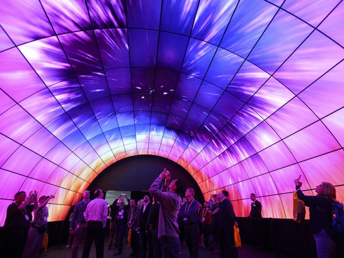 A picture of CES attendees looking above their head at a brightly illuminated arch made of digital displays
