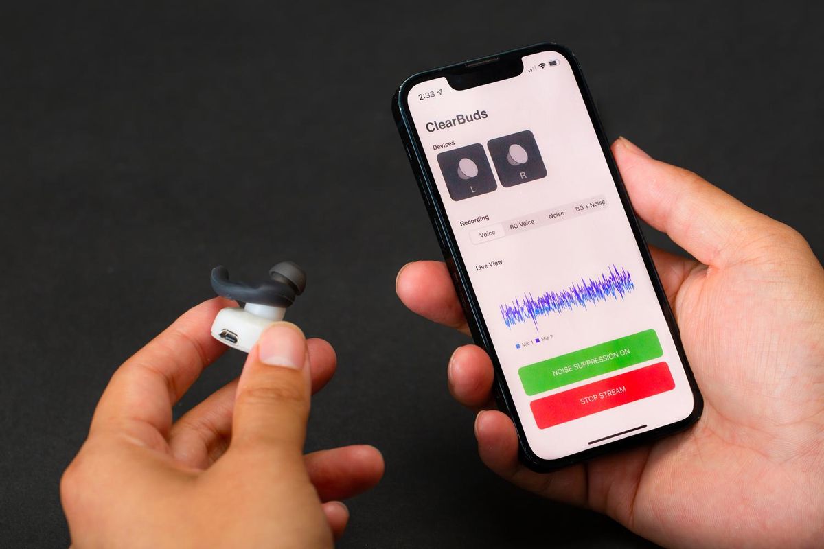 A picture of two hands. One holding a Clearbuds earbud, part of one of the first machine-learning systems to operate in real time and run on a smartphone. The other hand is holding a smartphone showing the ClearBuds app.