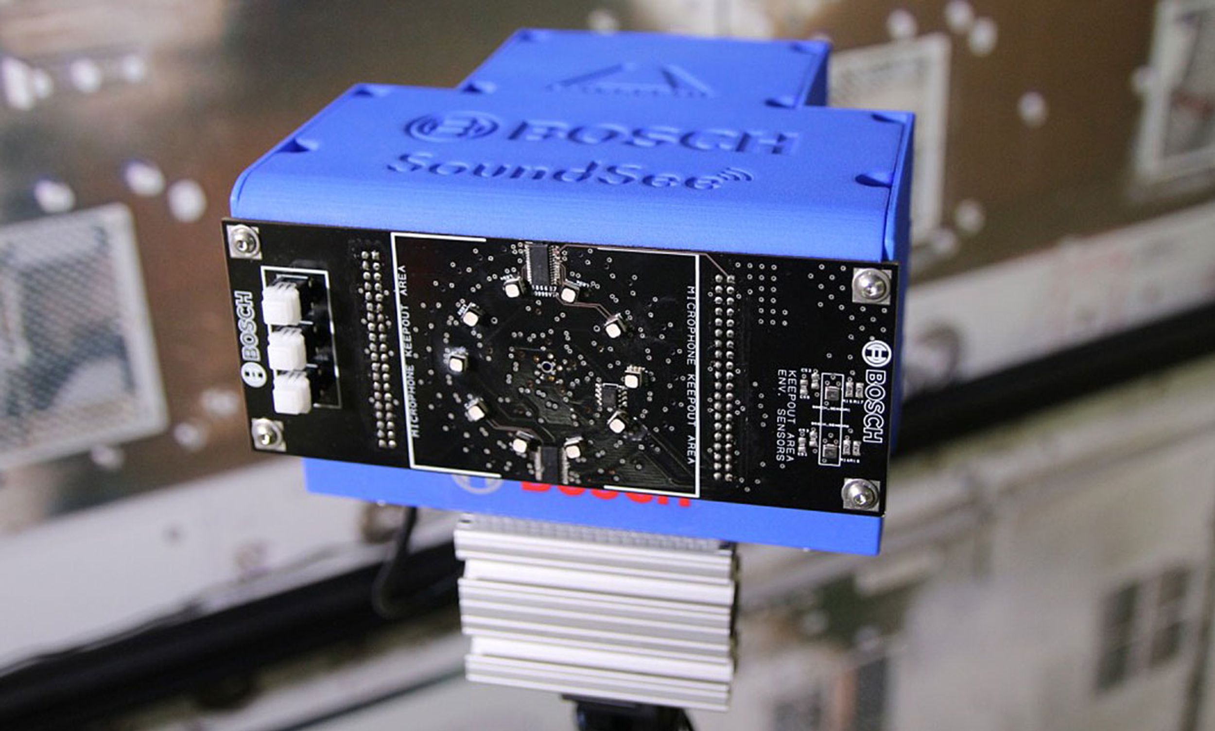 A rectangular blue box on a stand. The side closet to the viewer is covered with black printed circuit board, in the middle of which is 10 small white raised dots arranged in a ring