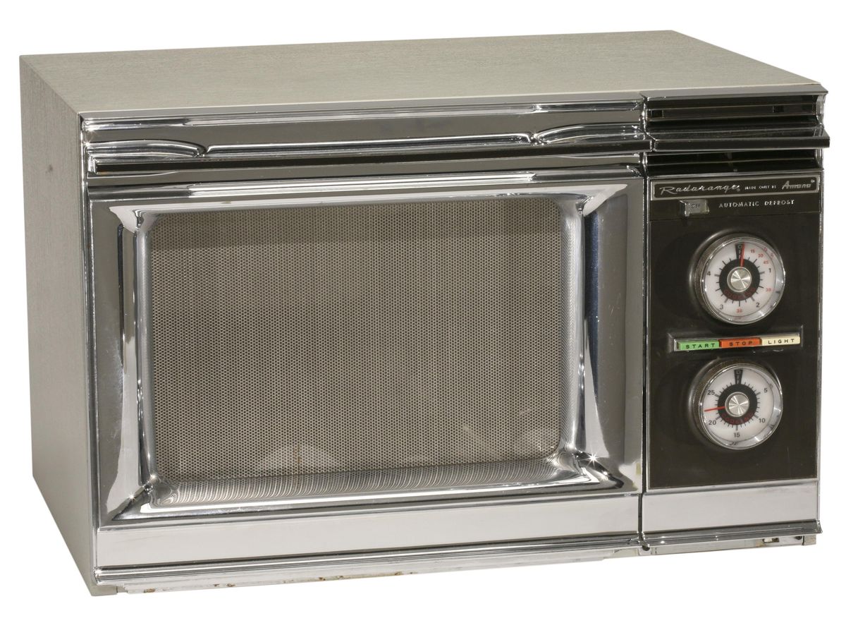 A rectangular kitchen appliance with a metal housing, a glass door, and two dials on the righthand side. 