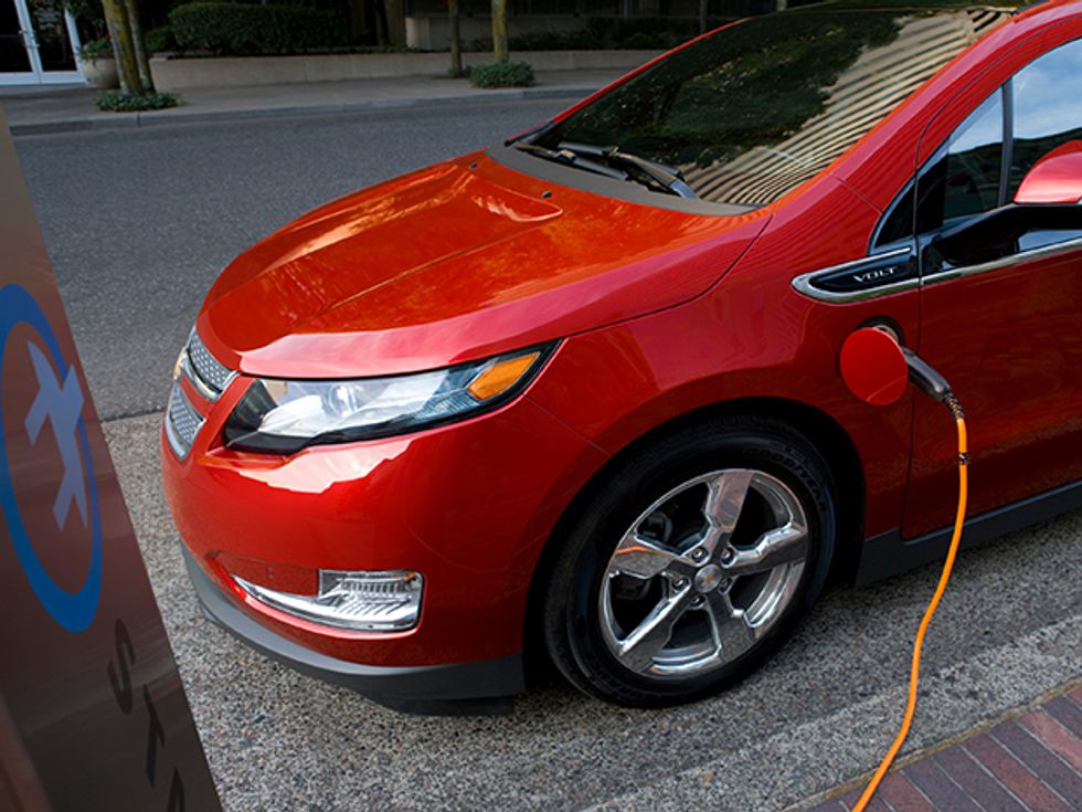 A red 2011 Chevy Volt plug-in hybrid-electric car being charged at a charging station.