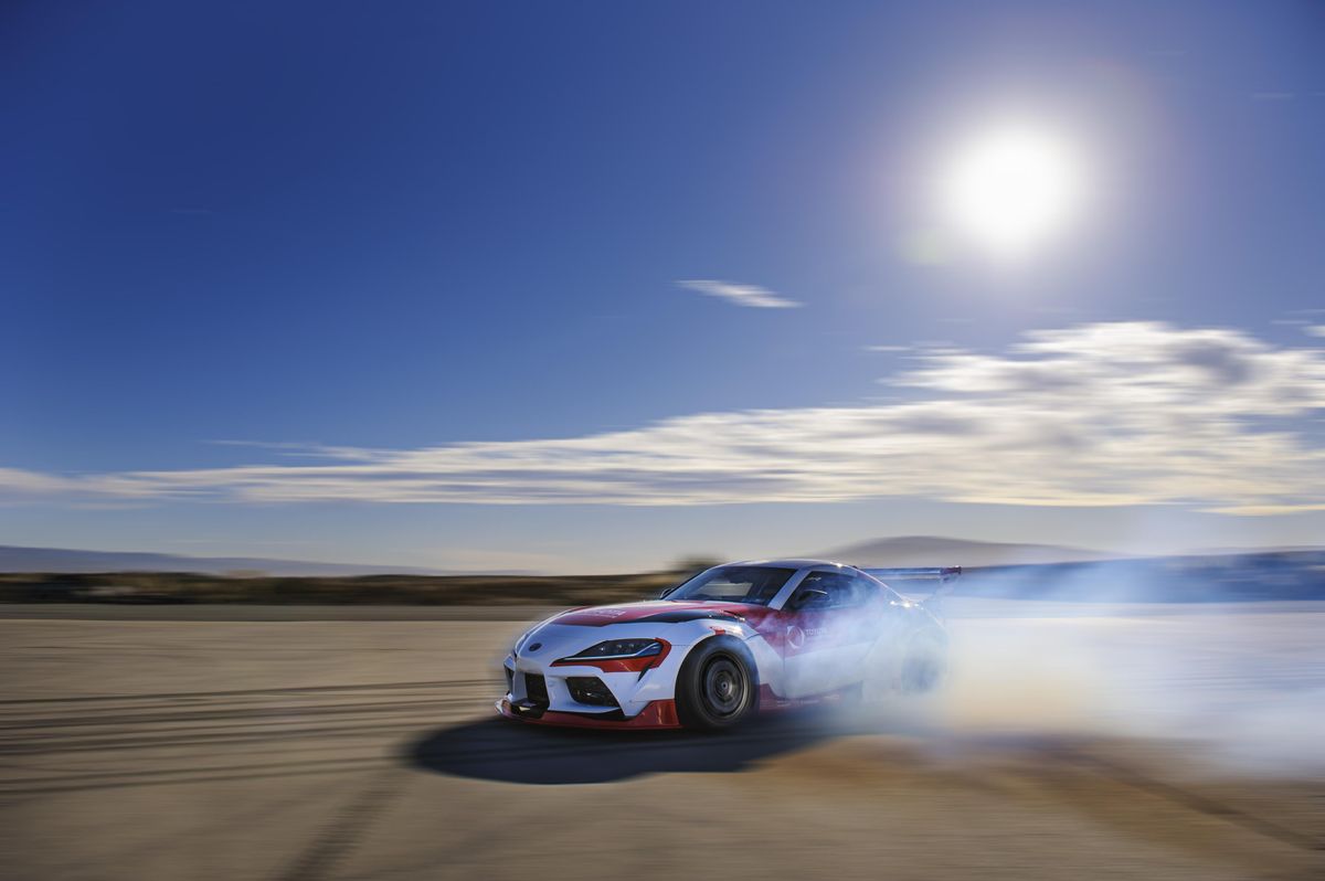 A red and white race car drifts sideways across a desert track with smoking tires
