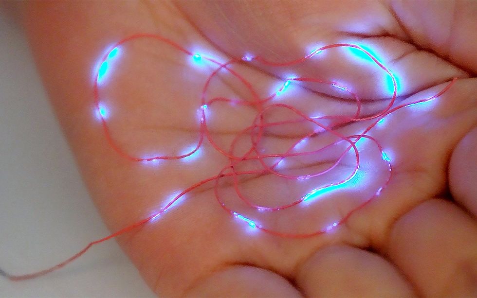 A red thread with glowing blue points along it sit in the palm of a hand.