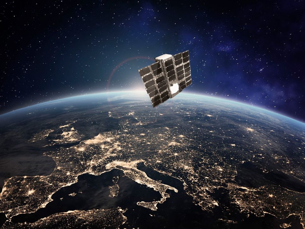 A rendering of a small satellite covered in black panels in orbit over Europe at night