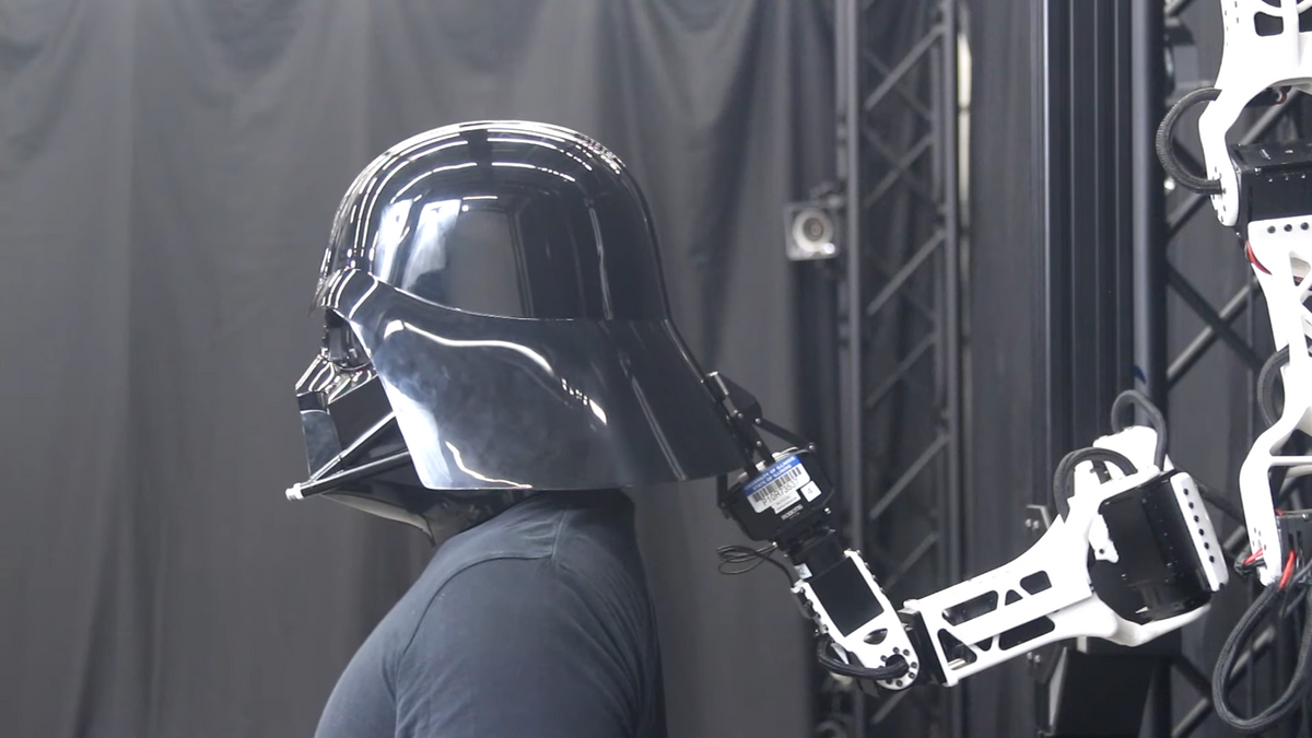 A robot arm lowers Darth Vader's helmet onto his head