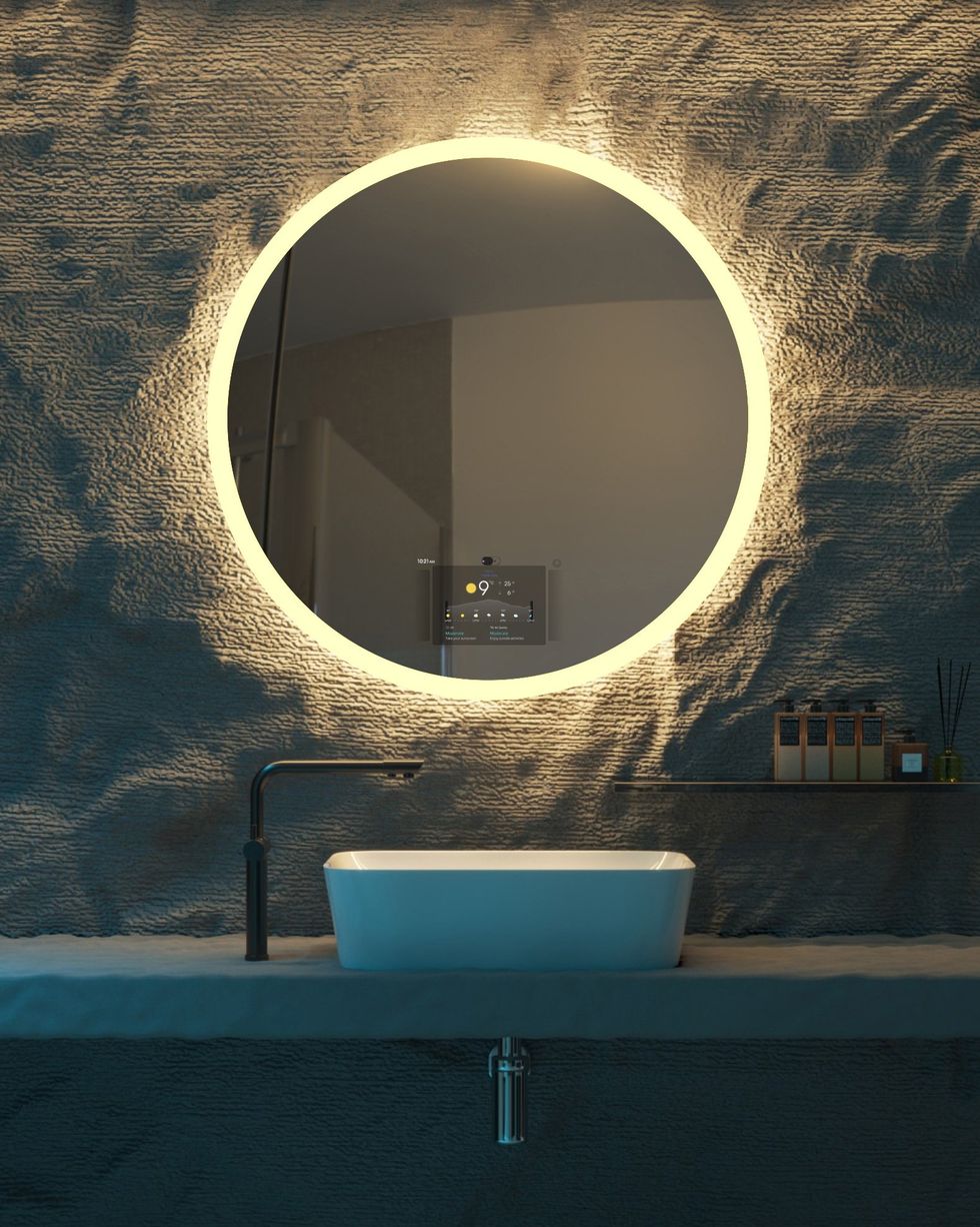 A round mirror surrounded by light above a sink.