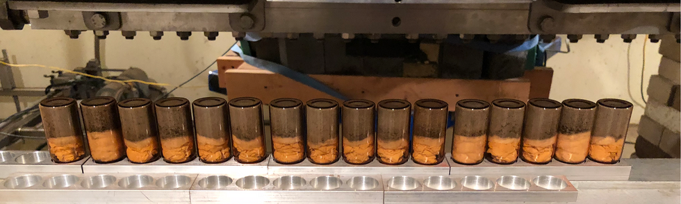 A row of upside down vials on a metal rack. The vials are amber-colored and contain metal chunks on top of chemical wipes.