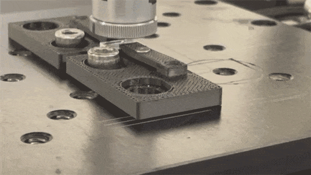Ein kurzes Video zeigt einen Femtosekundenlaser, der auf einer Werkbank ein kreisförmiges Objekt zu einem größeren Rechteck verschweißt.