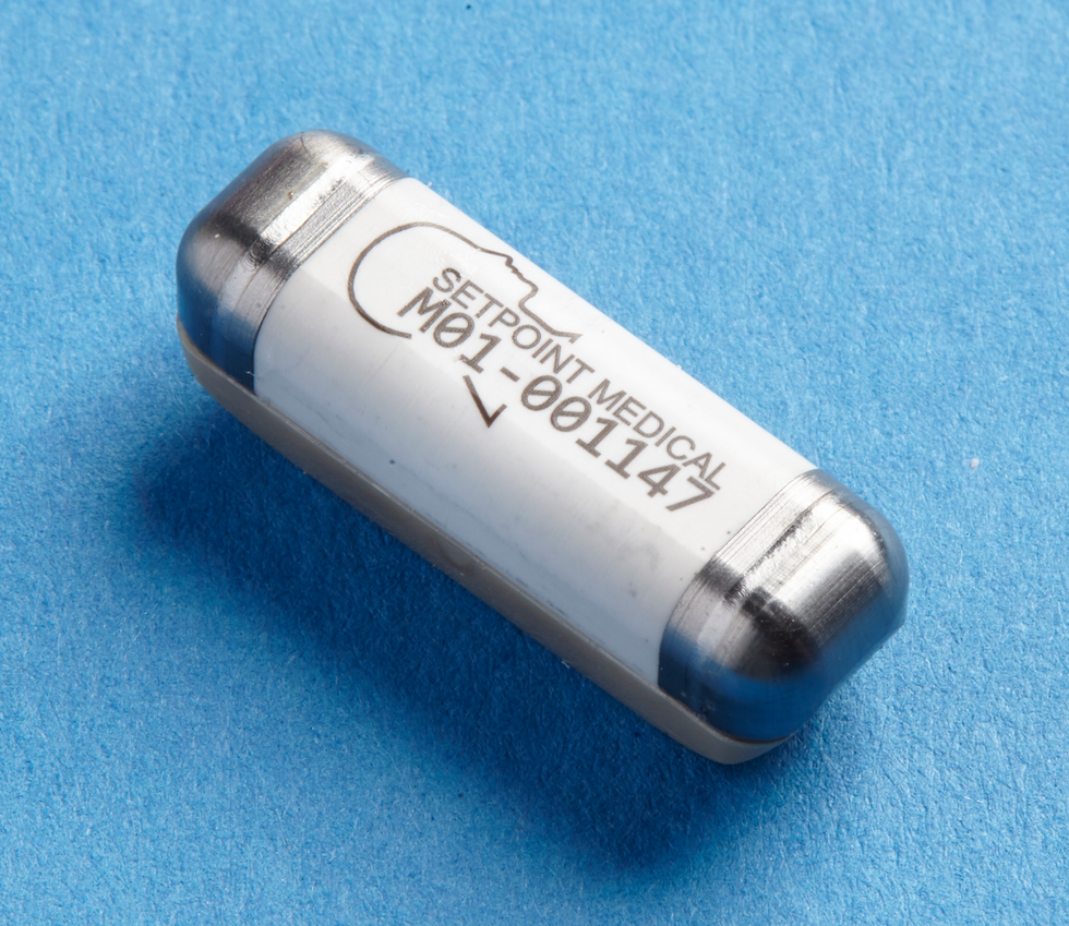 A silver and white capsule-shaped object lies on a blue background. Writing is on the white part.