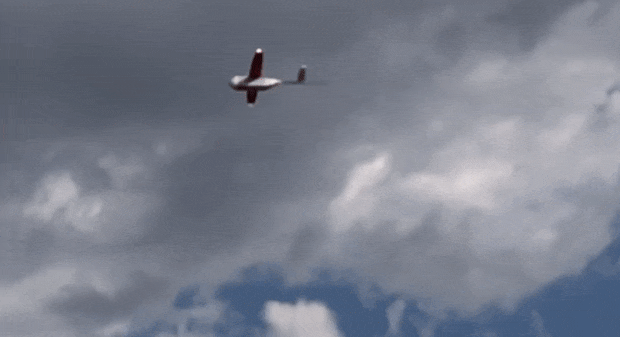 A small fixed-wing drone flies through the sky and drops a package with a parachute attached
