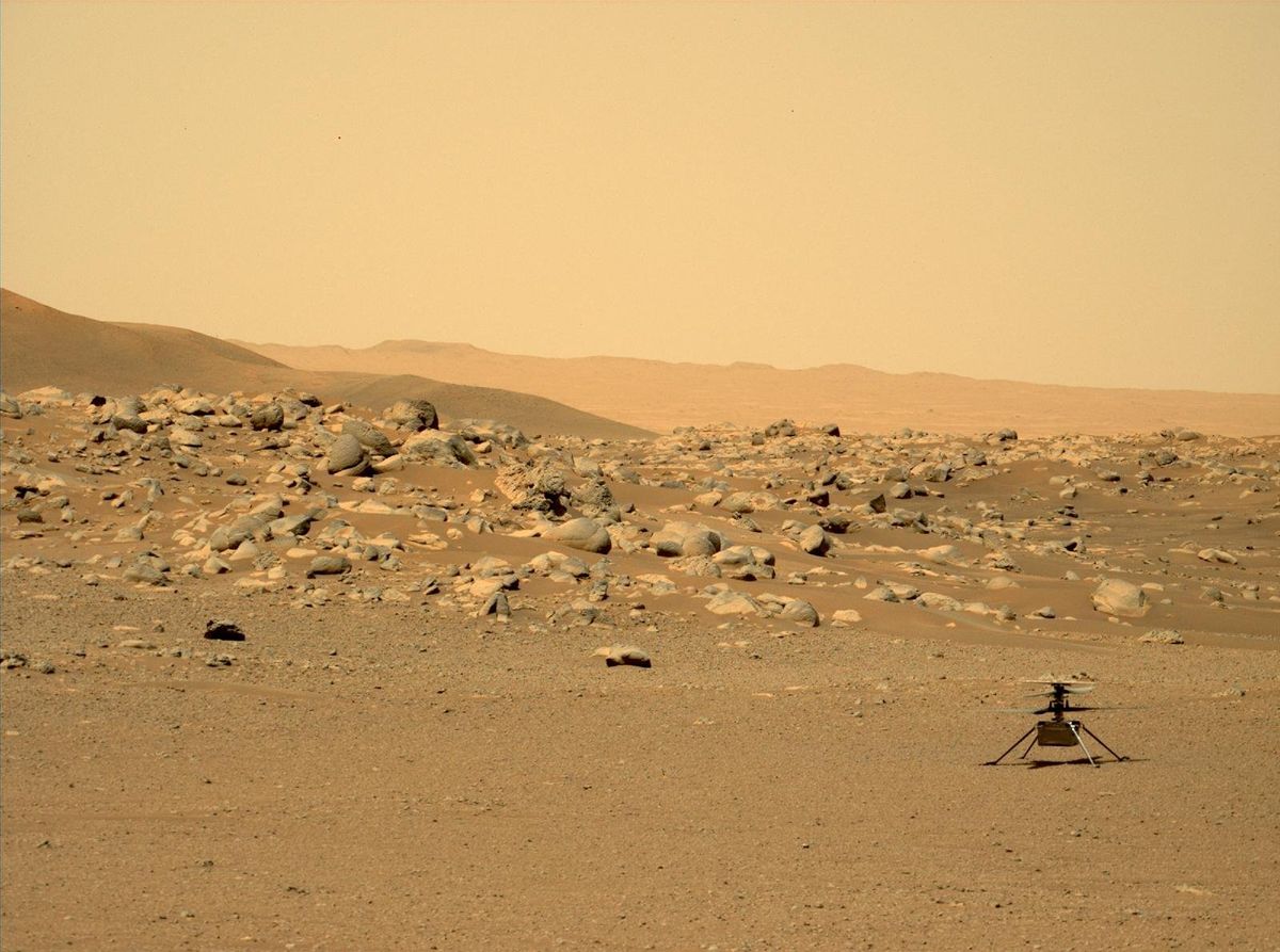 A small helicopter sits on the dusty, rocky surface of Mars
