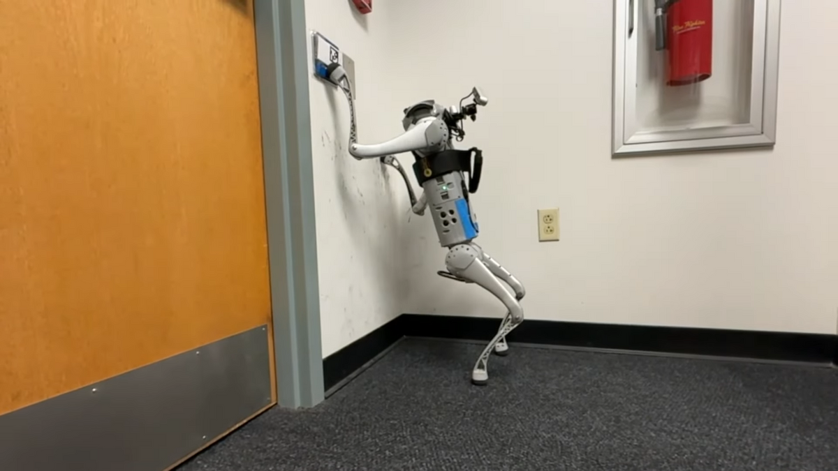 A small quadrupedal robot balances on two legs against a wall and uses one of its front legs to push a button to open a door
