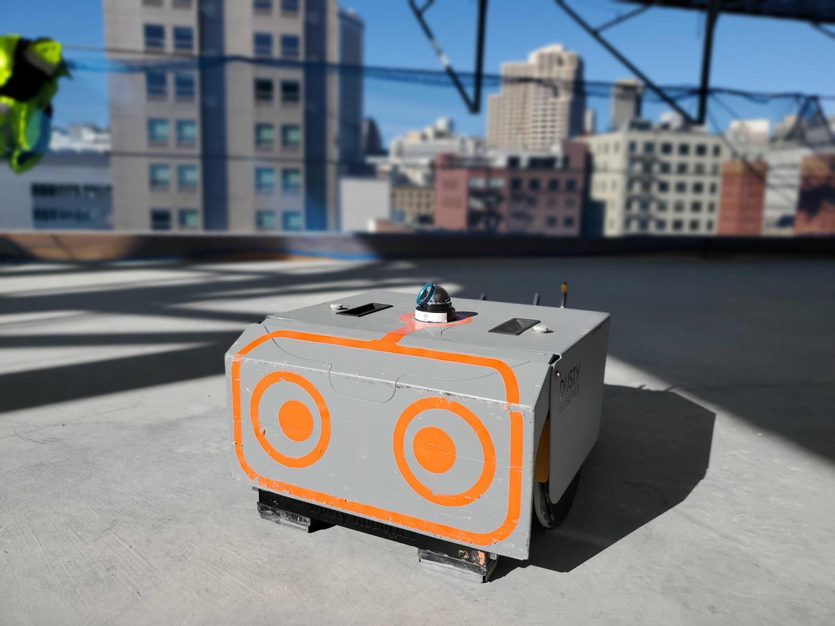 A small rectangular robot with large orange cartoon eyes on a construction site