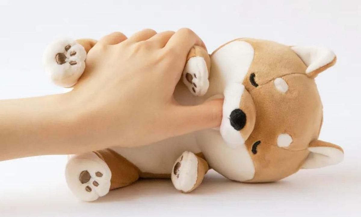 A small stuffed shiba inu sucks on a person's thumb