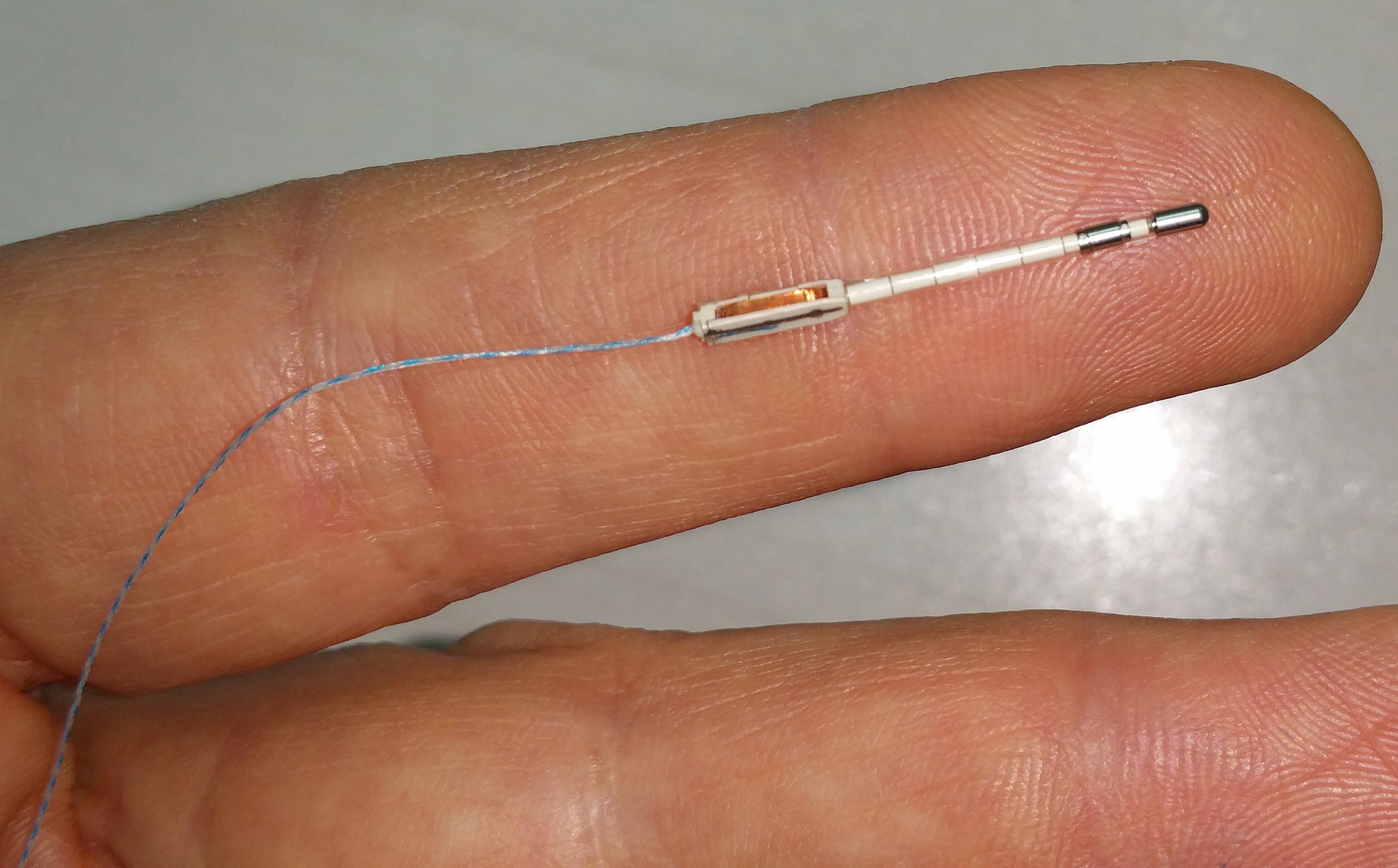 A small thin device with a metal cap on one end and a thin wire on the other sits in the middle of a finger.