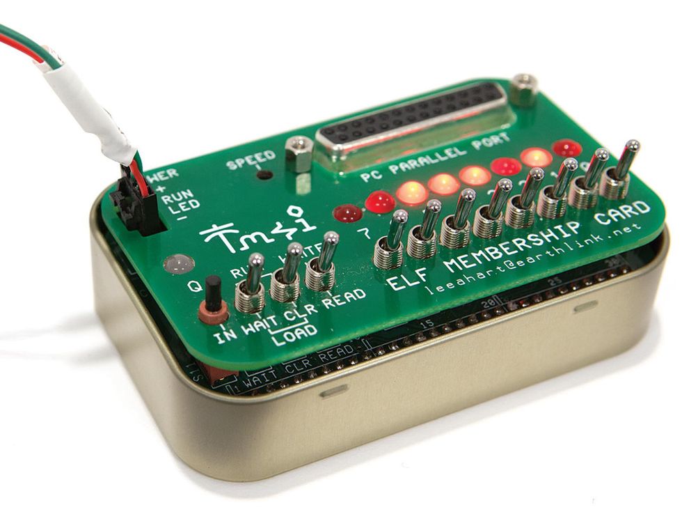 A small tin with a green board on top. The board has a series of toggle switches and LEDs.