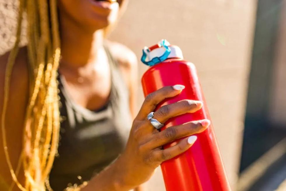 A smart ring on the finger of a woman holding a water bottle.