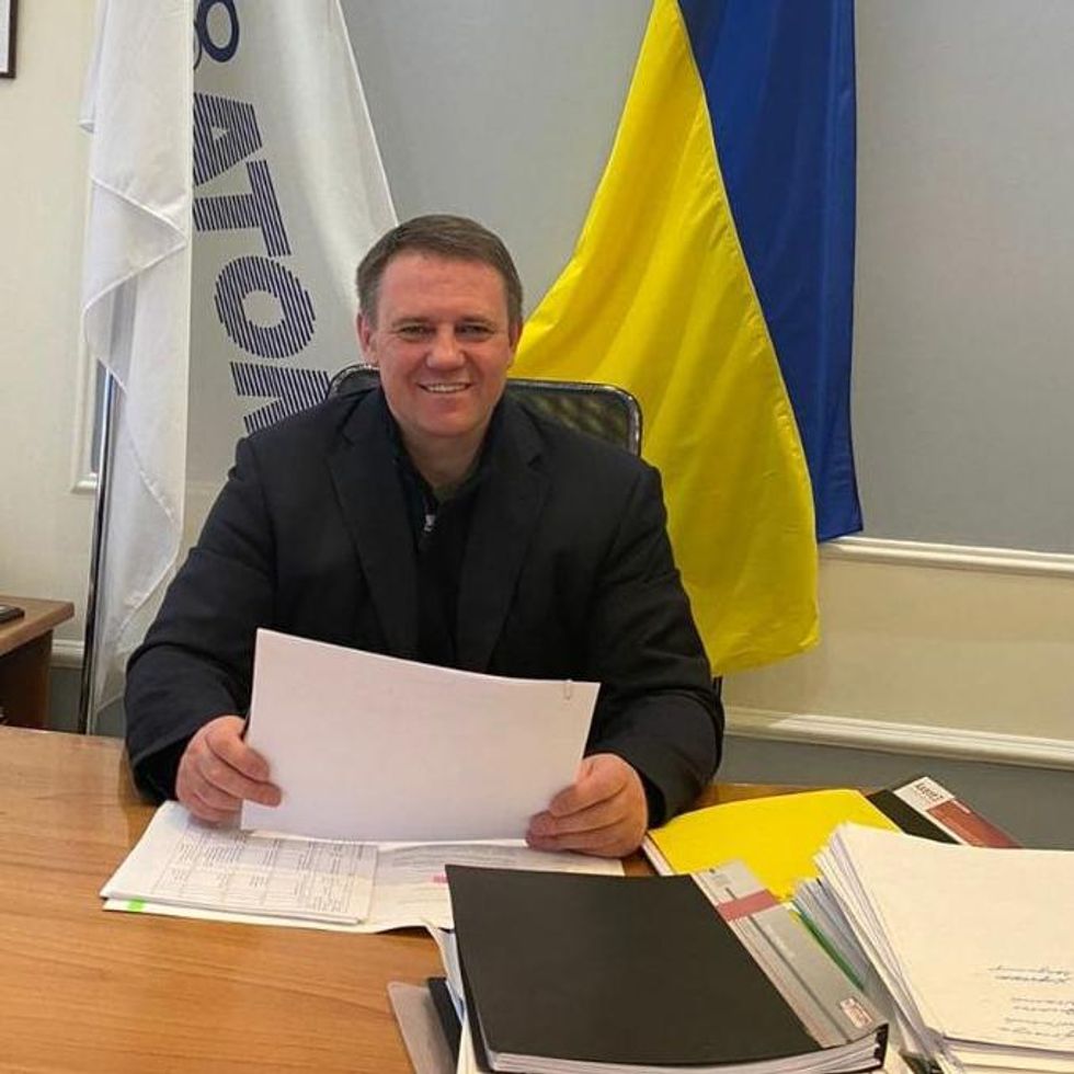 A smiling man at a desk in front of a Ukrainian flag