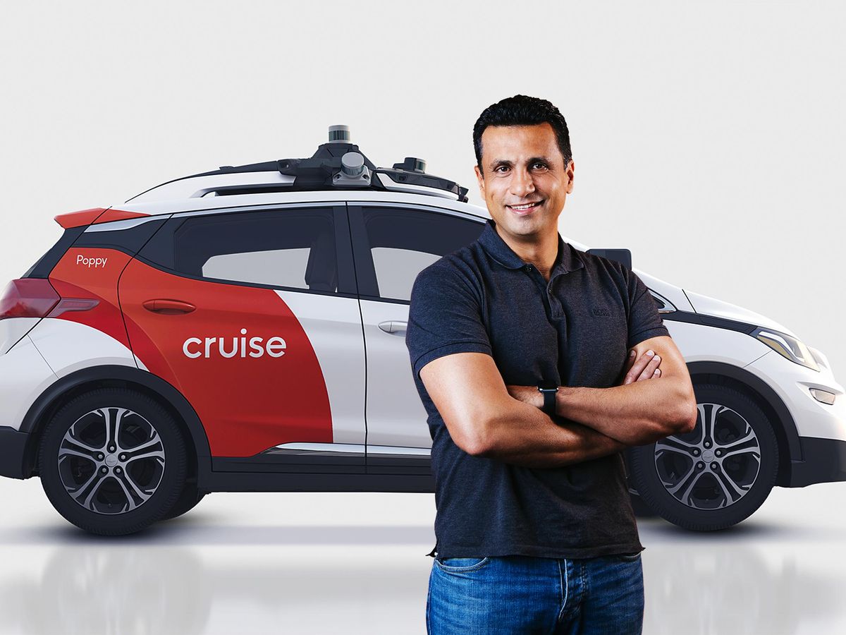 A smiling man in a black shirt and jeans in the foreground. Behind him is an autonomous car that says "cruise" on the side. 