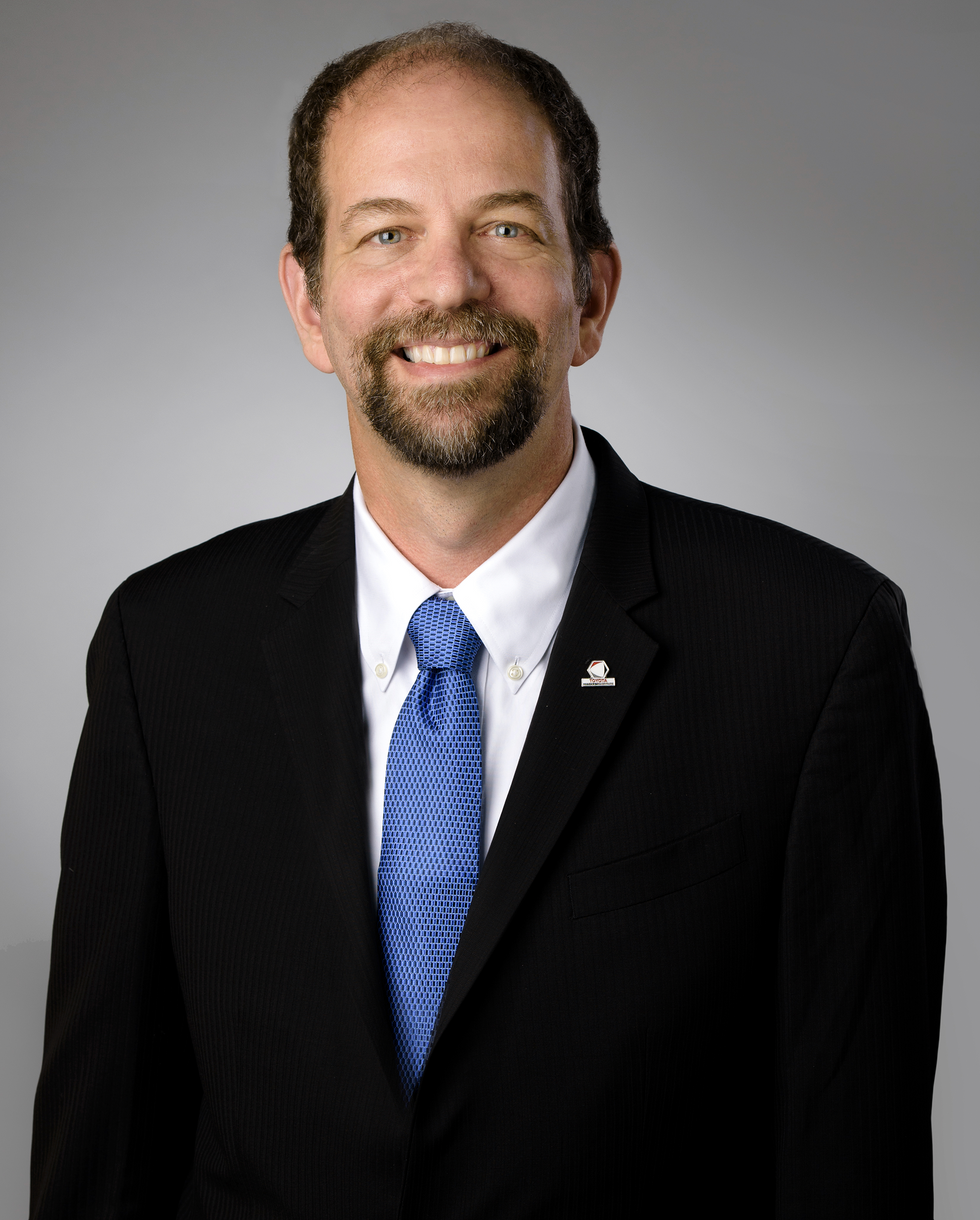A smiling man with a mustache and beard in a suit with a blue tie
