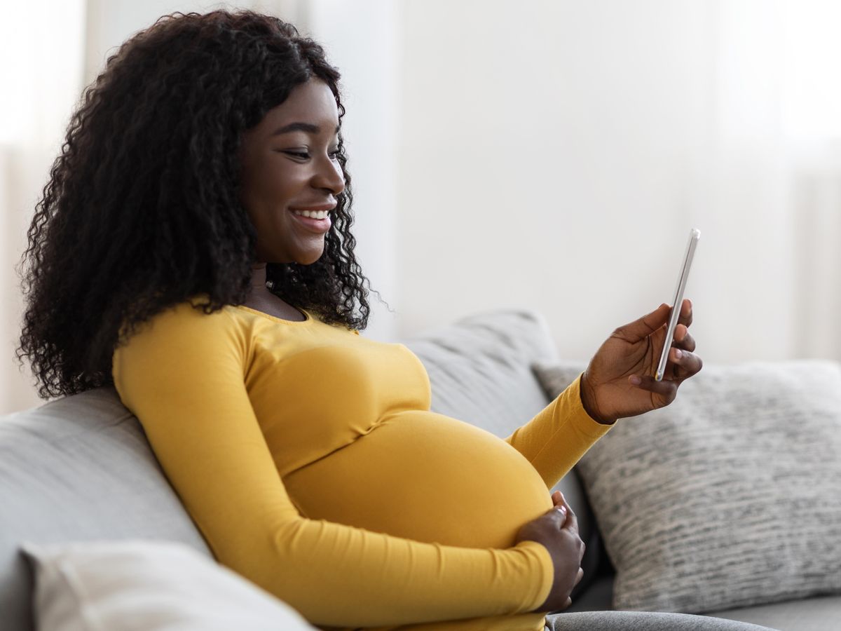 A smiling pregnant woman sitting on a couch and looking at her phone