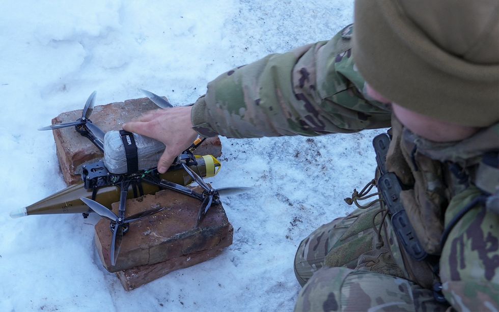 A soldier places his hand on a drone that carries a shell beneath it.