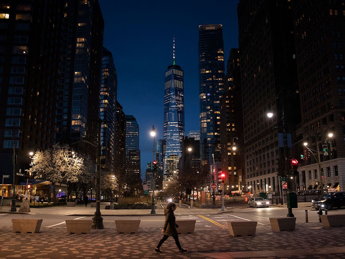 A solitary woman is seen walking in the foreground of the World Trade Center at night, New York, March 24, 2020