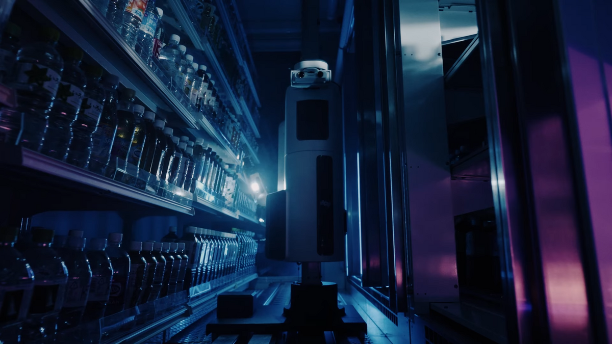 A tall and thin robot sits on a track inside of a convenience store beverage fridge