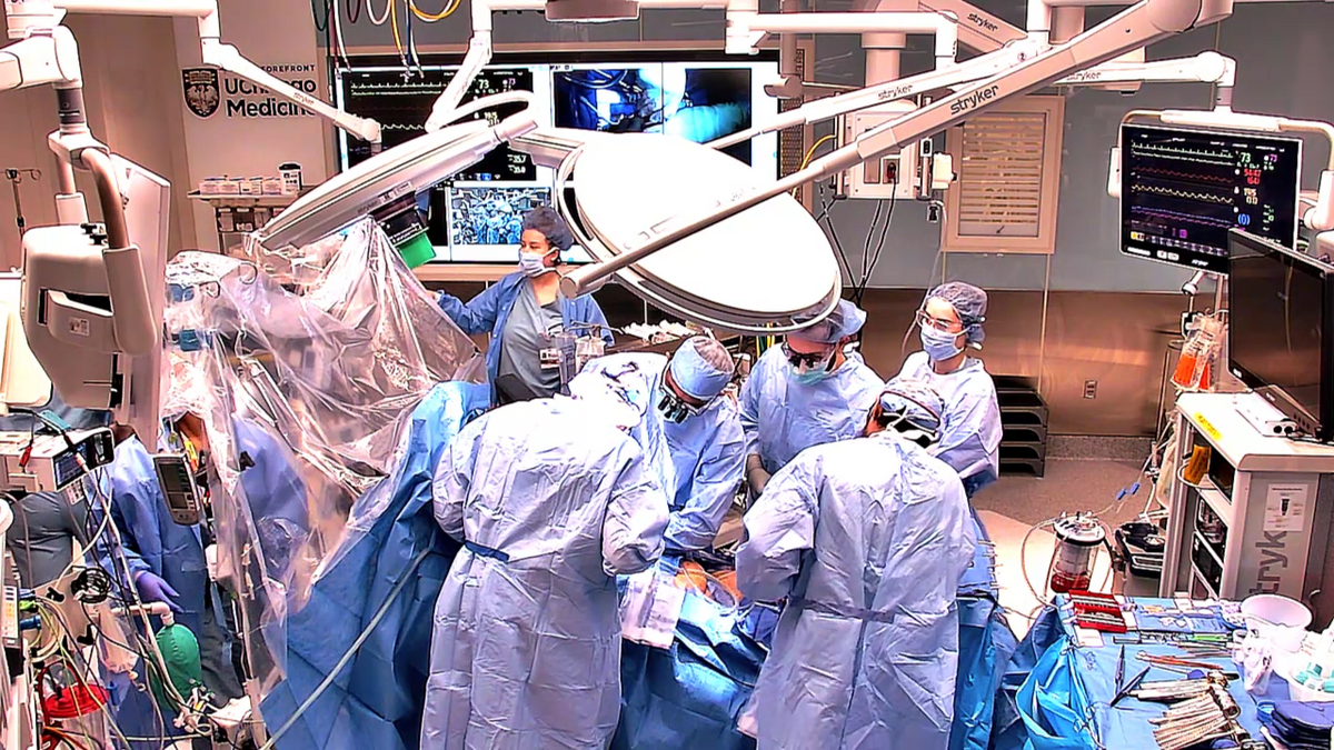 A team of doctors and nurses in scrubs is gathered around an operating table