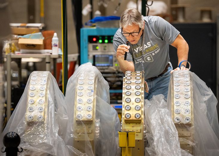 A technician examines a series of metal rings, 3 underneath plastic sheeting, one without