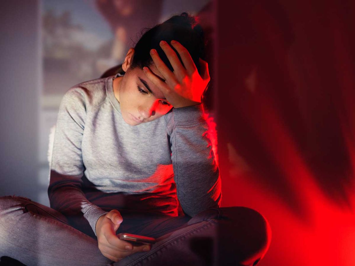 A teenage girl is using her smartphone in the dark room.