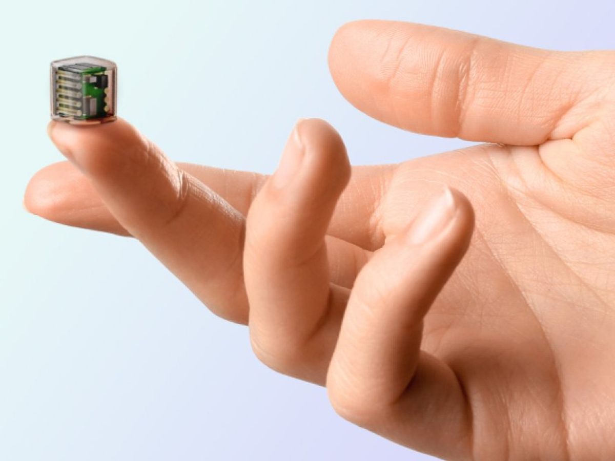A tiny cubical device is balanced on a fingertip. 