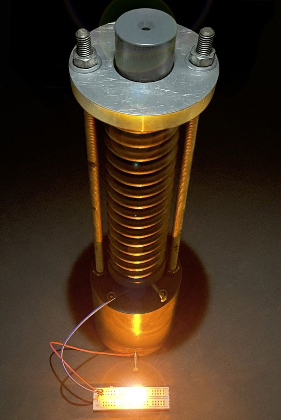 A tower of connected disks with a metal top and bottom connecting them, and wires linked to a glowing LED on a bread board.