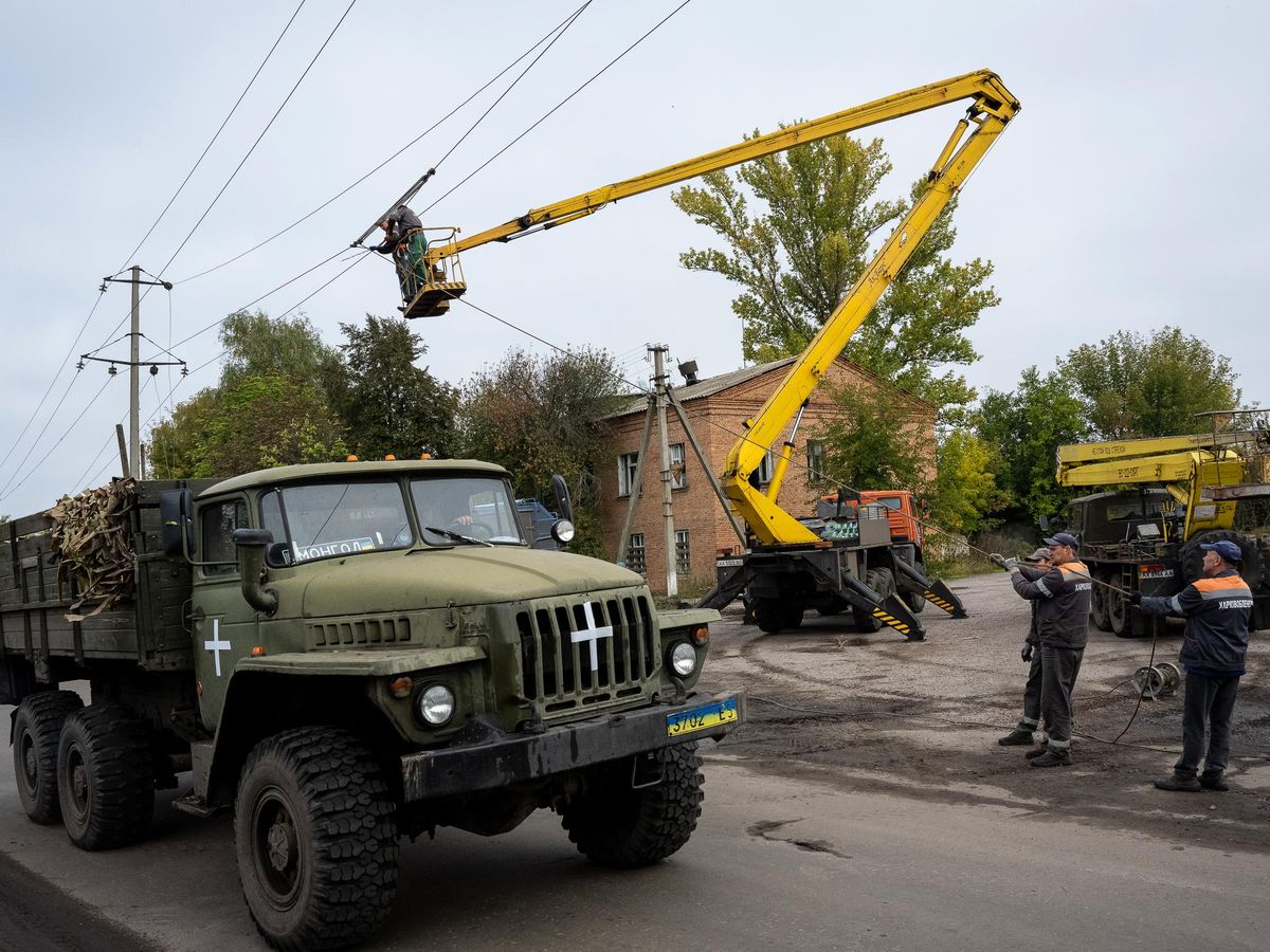 A truck with a Ukrainian license plate, and a vehicle with a cherry picker. Multiple workers fix electric wires on poles.