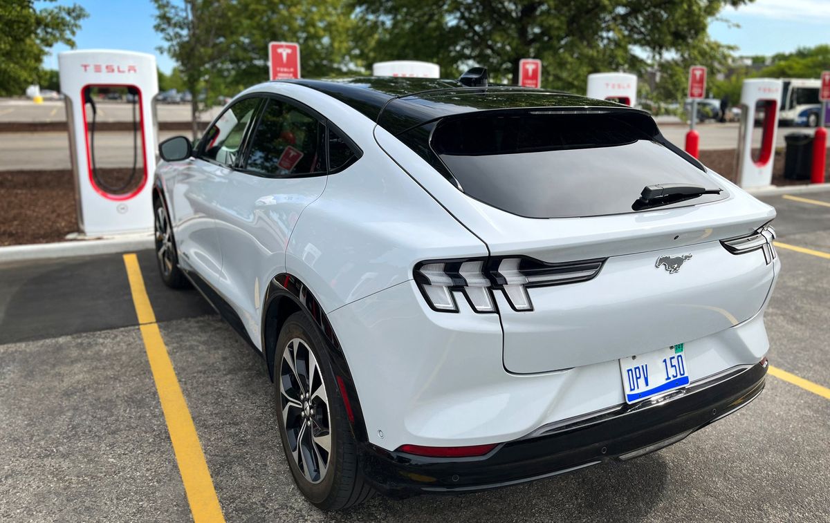 A white car is parked at an outdoor Tesla EV charging station.