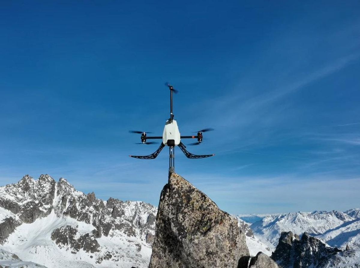 A white drone balances on top of a mountain with a mountain scene in the background