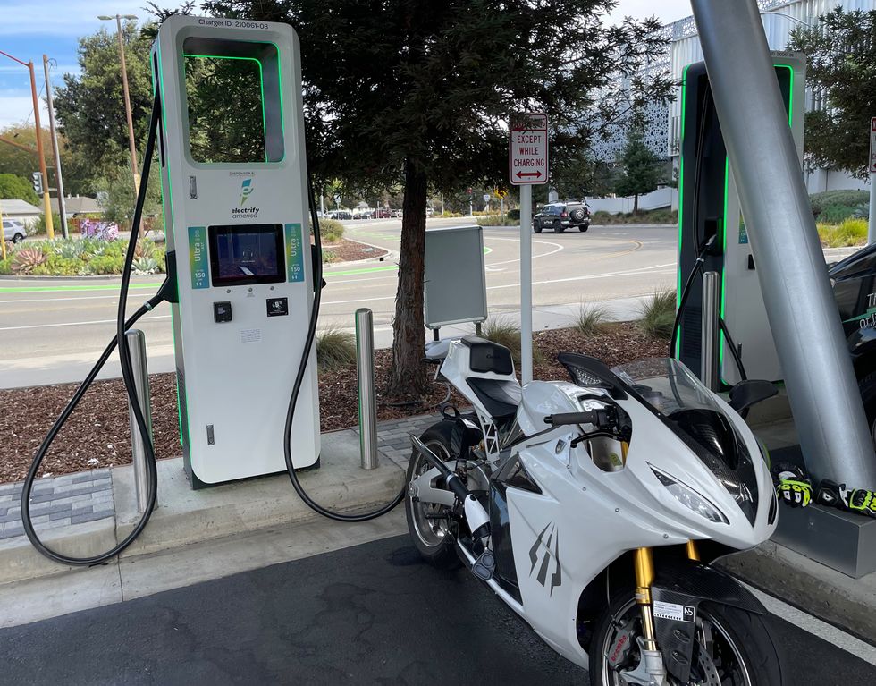 A white electric motorcycle charging in a parking lot.